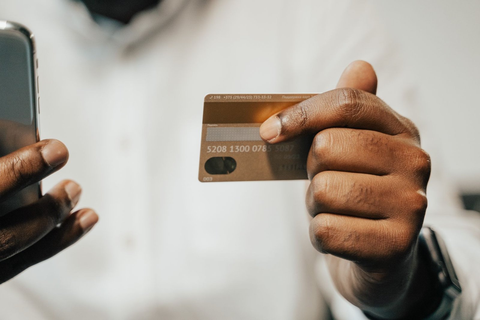 Pessoa segurando um cartão e o celular para fazer um pagamento