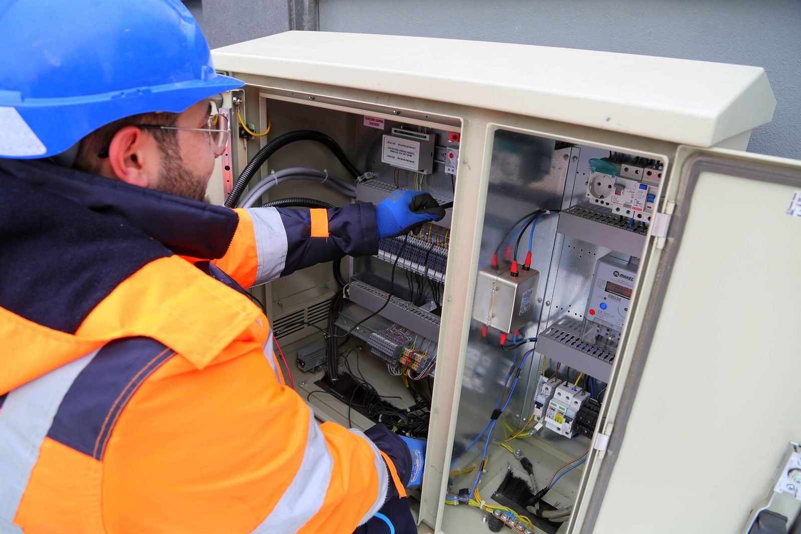 Eletricista com equipamento de proteção trabalhando em um quadro elétrico externo