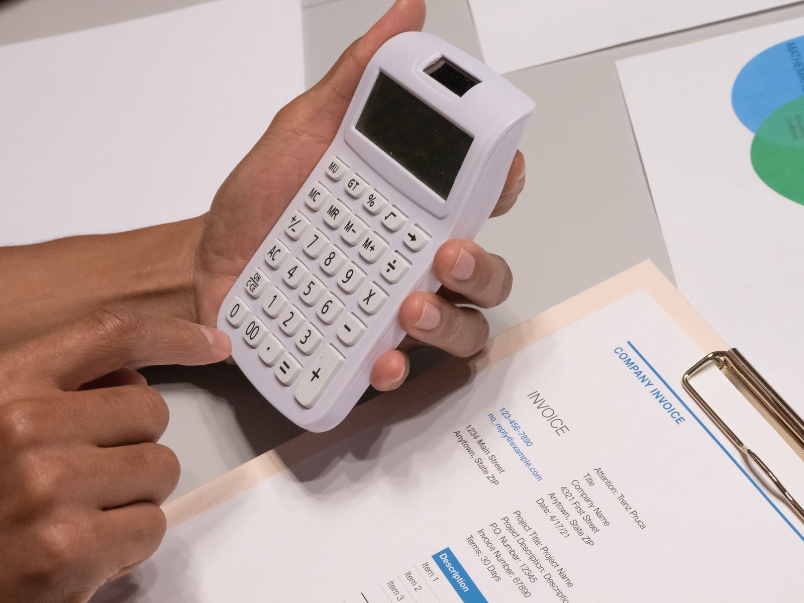 Mãos conferindo notas e documentos com a calculadora sobre a mesa