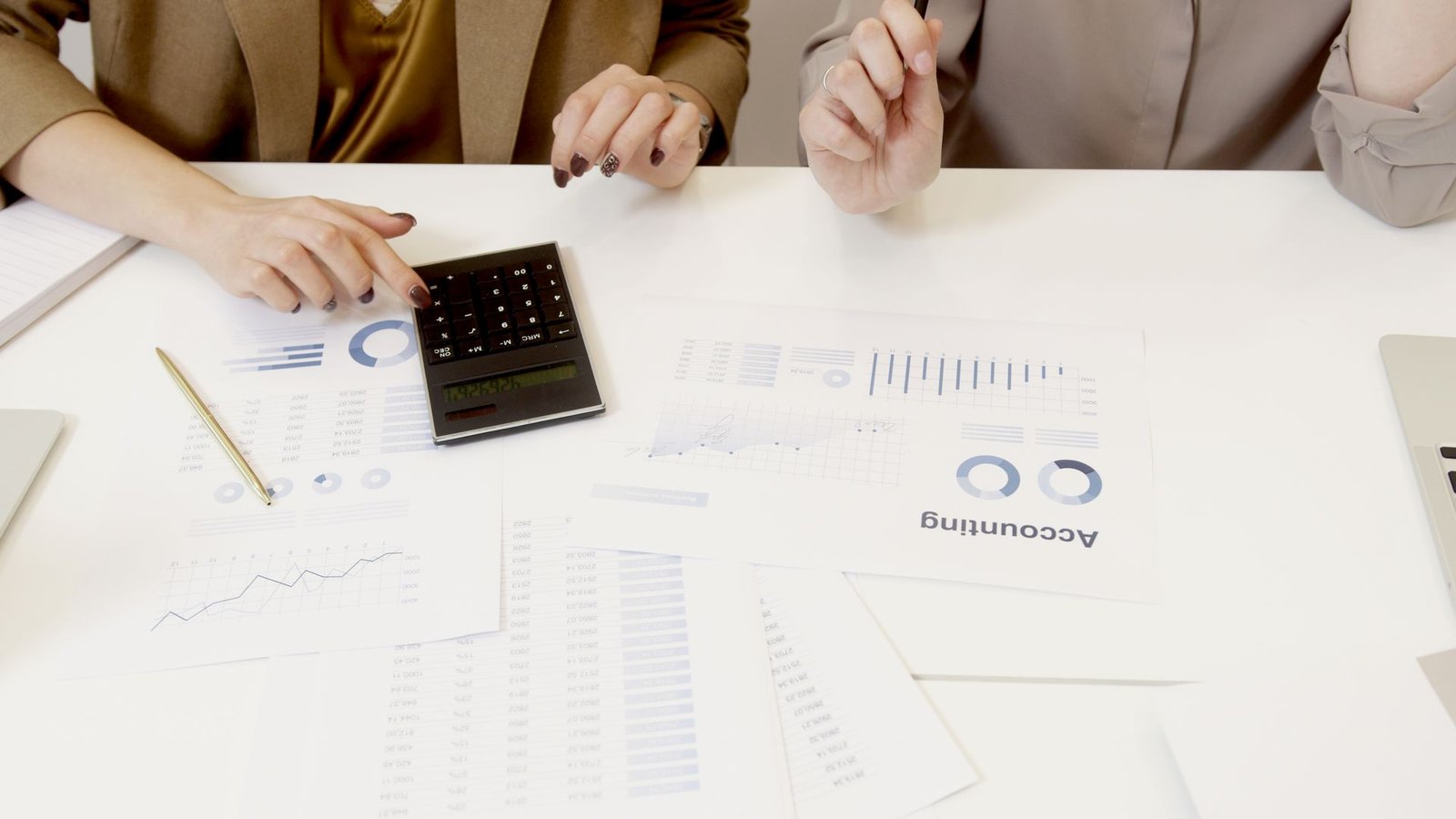 Profissionais comparando dois relatórios financeiros com a calculadora na mesa