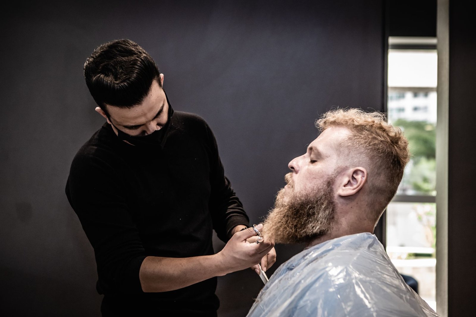 Barbeiro aparando a barba de um cliente em uma barbearia moderna